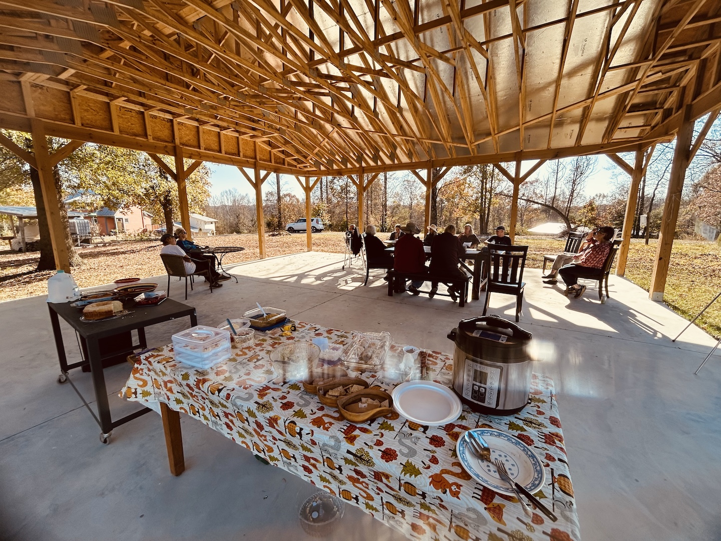 People gathered under a wooden pavilion in an ecovillage setting.