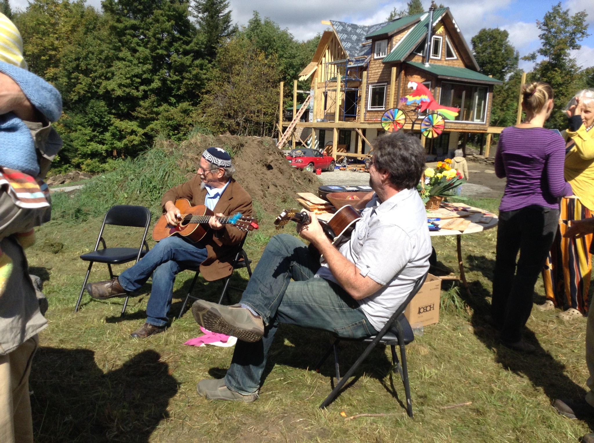 People playing guitar at outdoor community event with a house in the background.