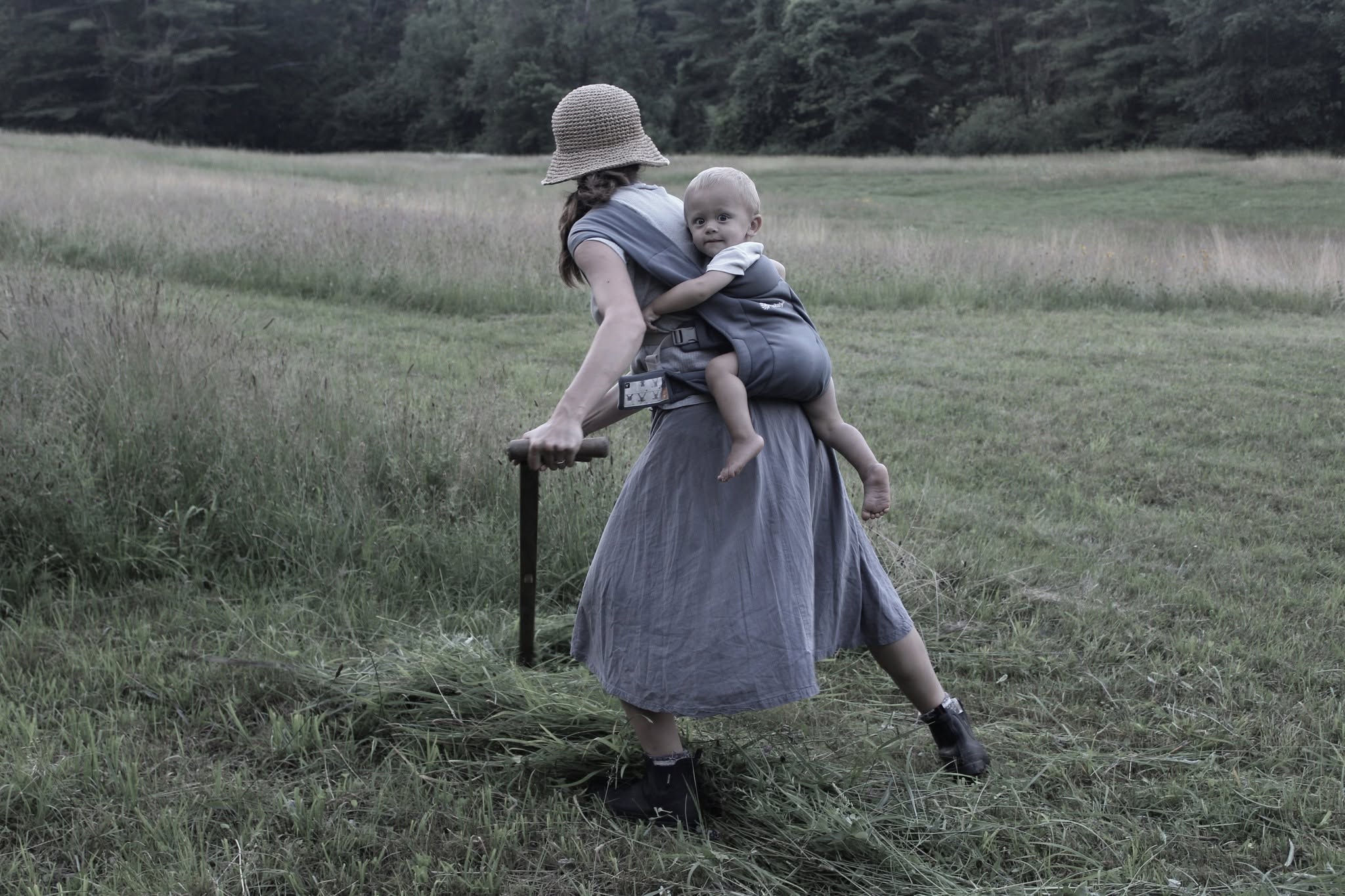 Woman with a child in a baby carrier walking in a grassy field.