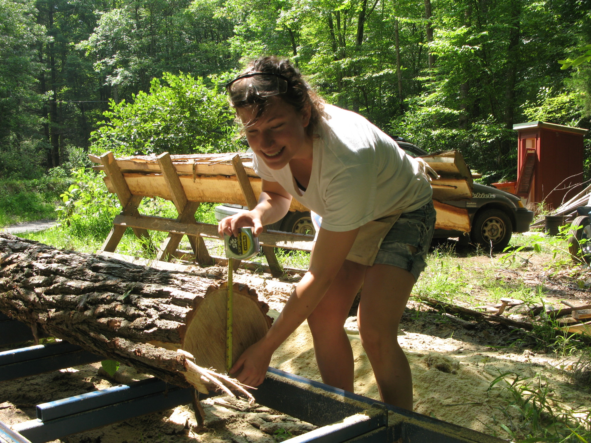 Woman measuring a log for a woodworking project in a forest setting.