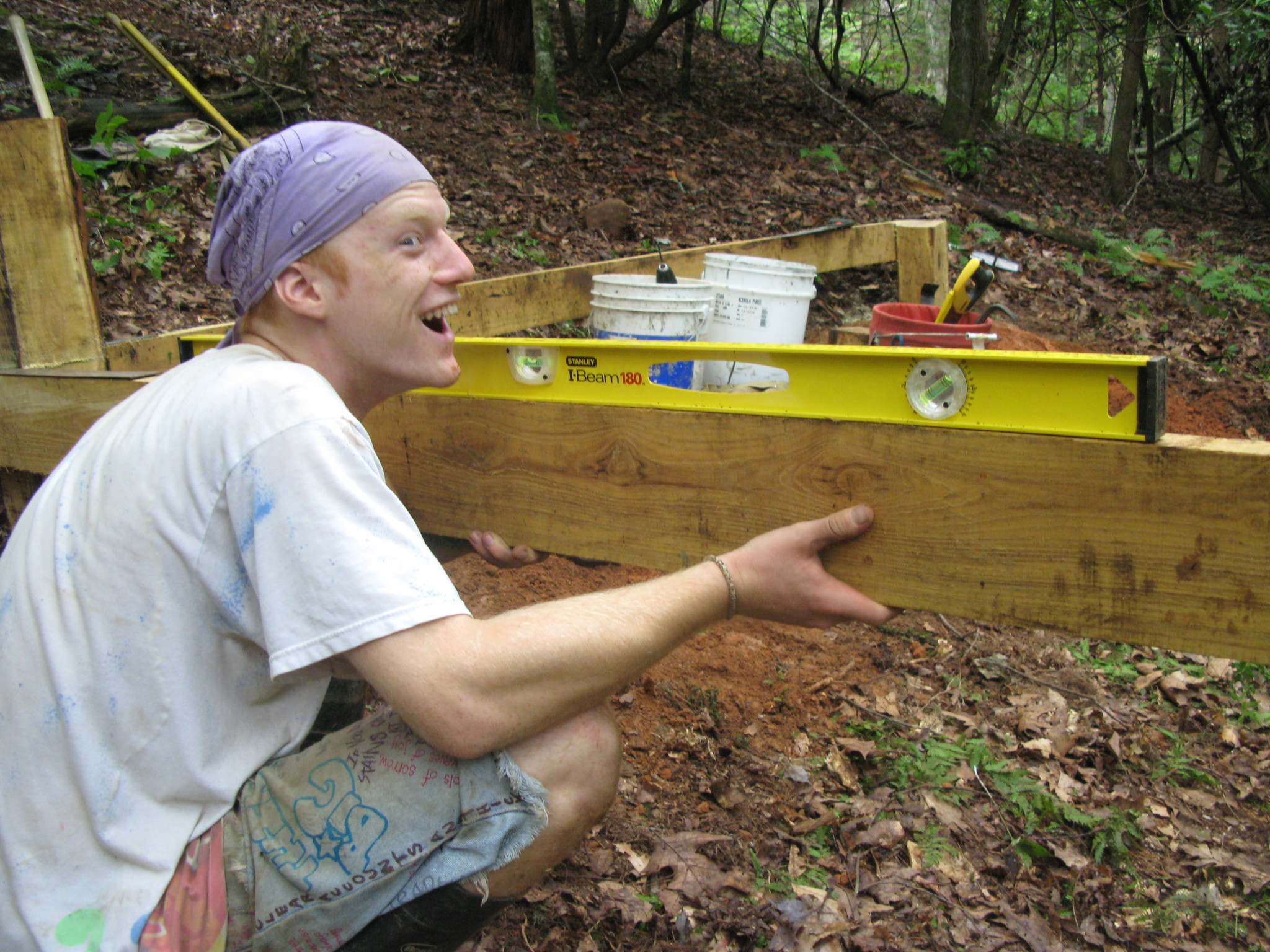 Person installing a wooden raised garden bed in a forested area.