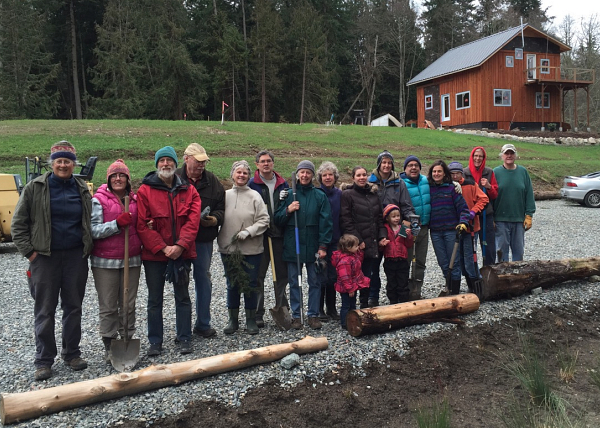 Group of people outdoors at a community event near a wooden house.