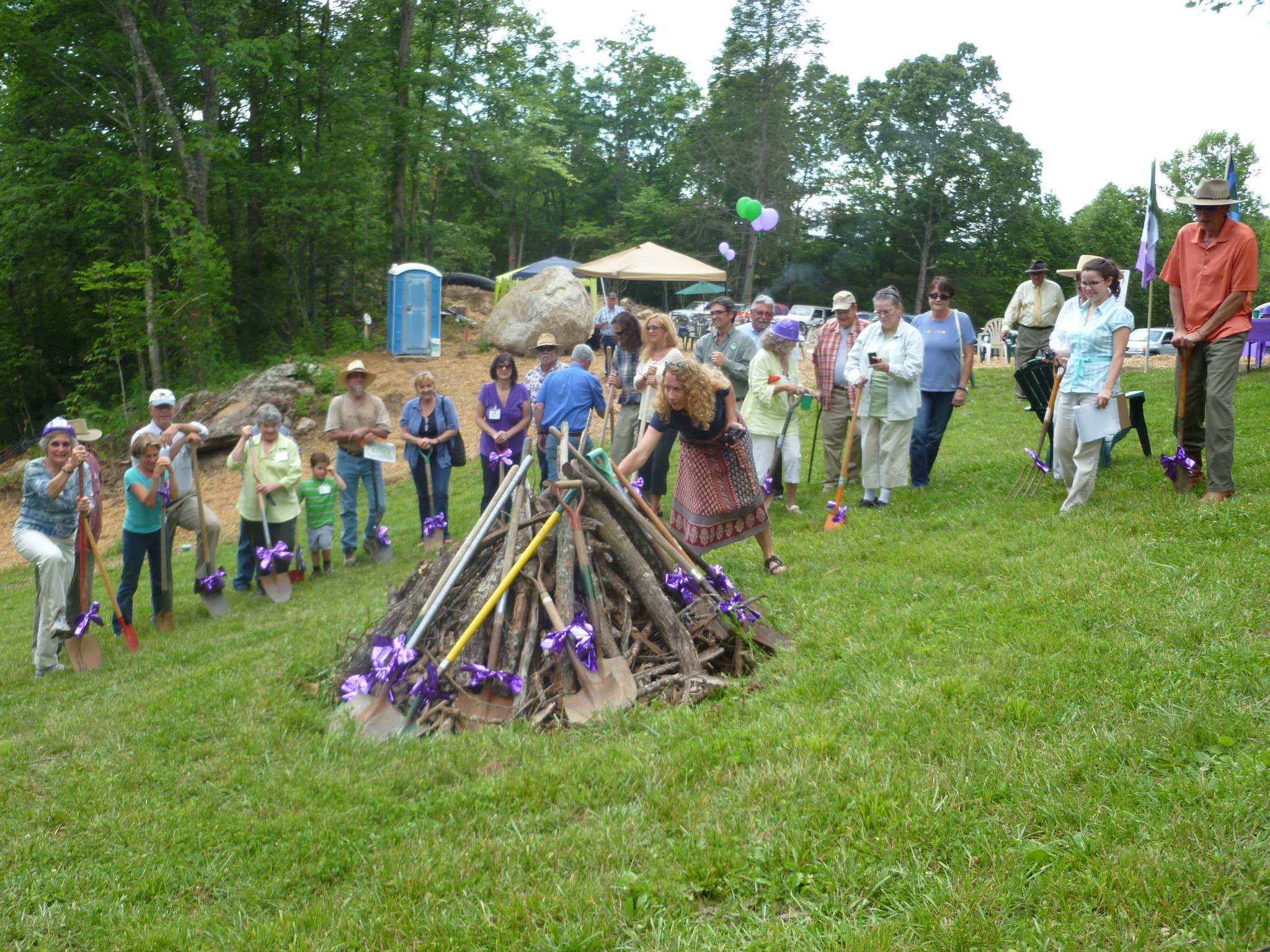 People gathered around a bonfire in a lush green outdoor setting.