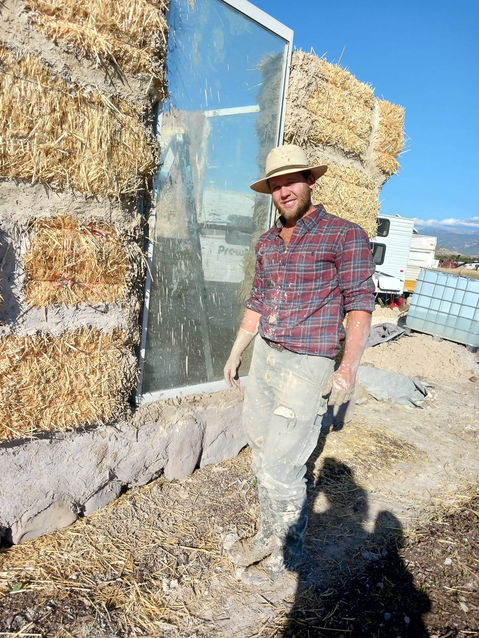 Man standing outdoors at Earthen Grove Ecovillage with straw bales and glass wall.