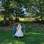 Bride walking with two bridesmaids in a lush green outdoor setting.