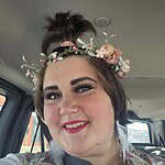Smiling woman wearing a floral crown and colorful outfit in car.