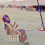 Woman enjoying swing chair at Burning Man festival in desert landscape.