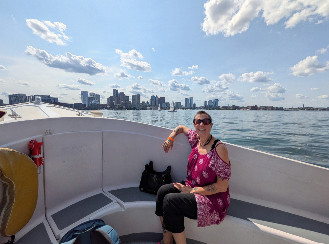 Woman smiling on boat with city skyline and water in background.