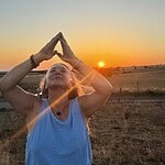 Woman doing yoga outdoors during sunset in an open field.