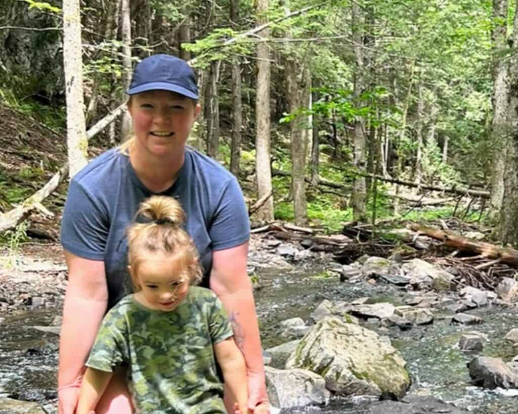 Woman and child exploring a forest stream in a lush green woodland.