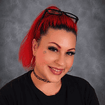 Portrait of a woman with red hair, glasses, and a black T-shirt.