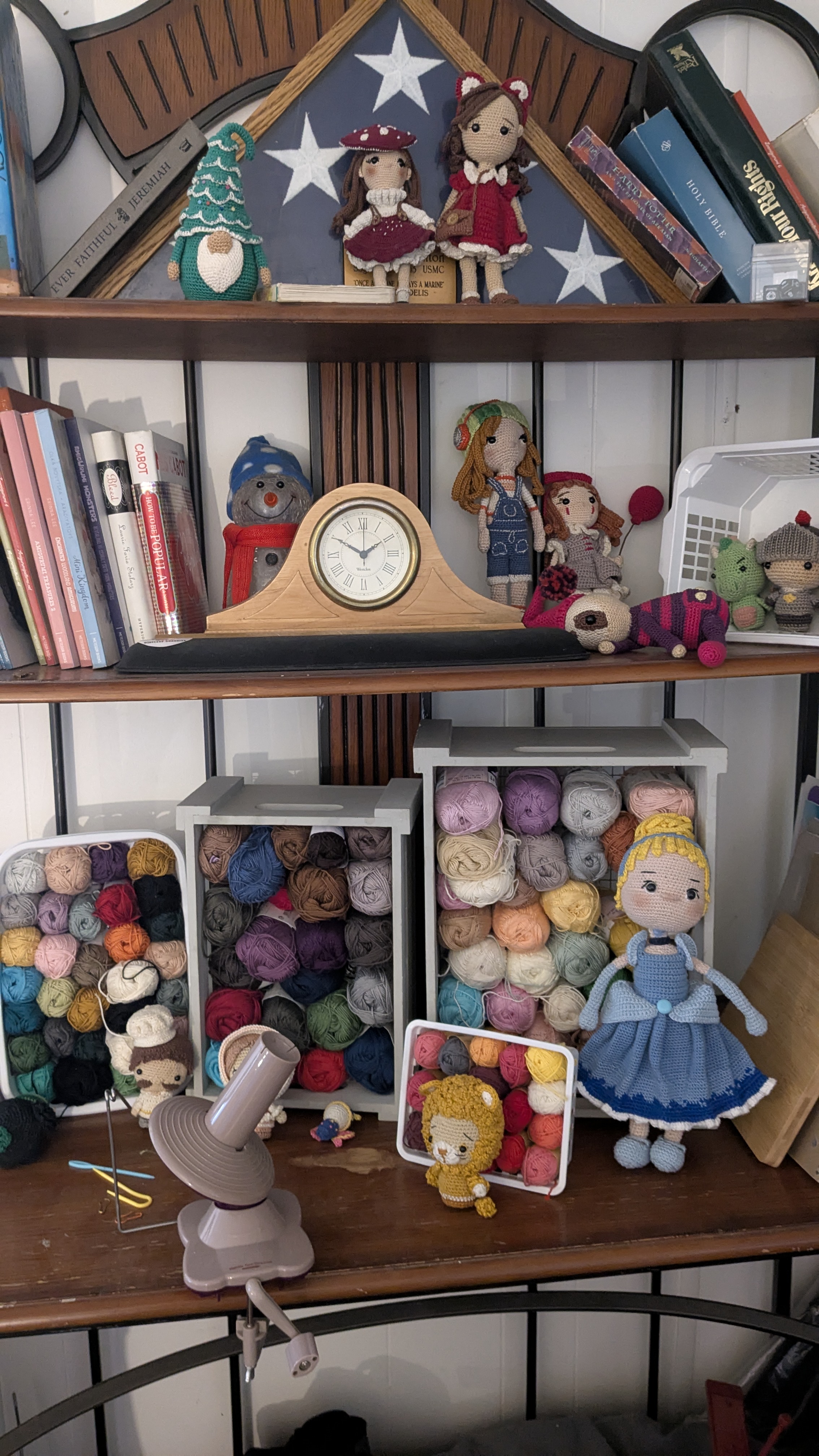 Shelf filled with yarn, dolls, books, and crafting supplies in a cozy room.