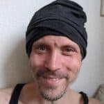 Smiling man wearing a black headwrap and tank top, close-up portrait.
