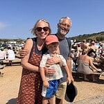Happy family at community event with outdoor picnic tables and sunny sky.