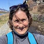 Smiling woman with sunglasses and backpack on a riverside trail.