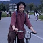 Smiling person riding a bicycle at outdoor community gathering.