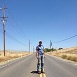Person standing on a rural road with power lines and open fields.