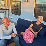 Two community members relaxing on a cruise ship deck with large windows.