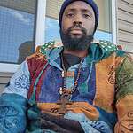 Portrait of a man wearing colorful hoodie and wooden cross necklace.