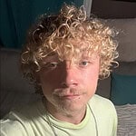 Close-up of a young man with curly blonde hair and blue eyes.