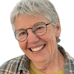Smiling woman with glasses and short gray hair, wearing a plaid shirt.