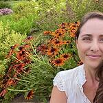 Woman smiling in garden with vibrant orange and yellow flowers.