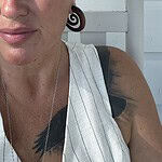 Close-up of a woman with tattoos and earrings, smiling outdoors.