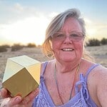 Smiling woman holding a geometric object outdoors at sunset.