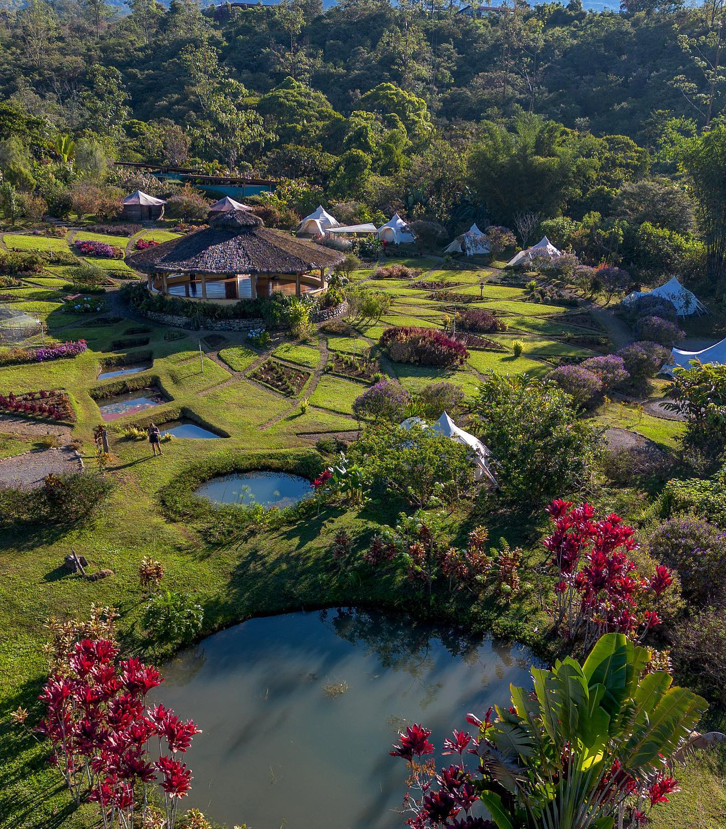 Beautiful community garden with ponds, lush greenery, and small structures in a hilly landscape.