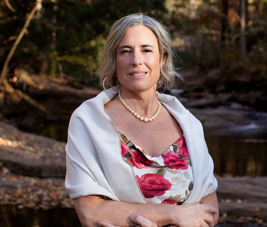 Woman smiling outdoors near a river, representing community and nature.