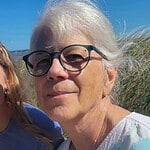 Senior woman with glasses outdoors at community gathering.