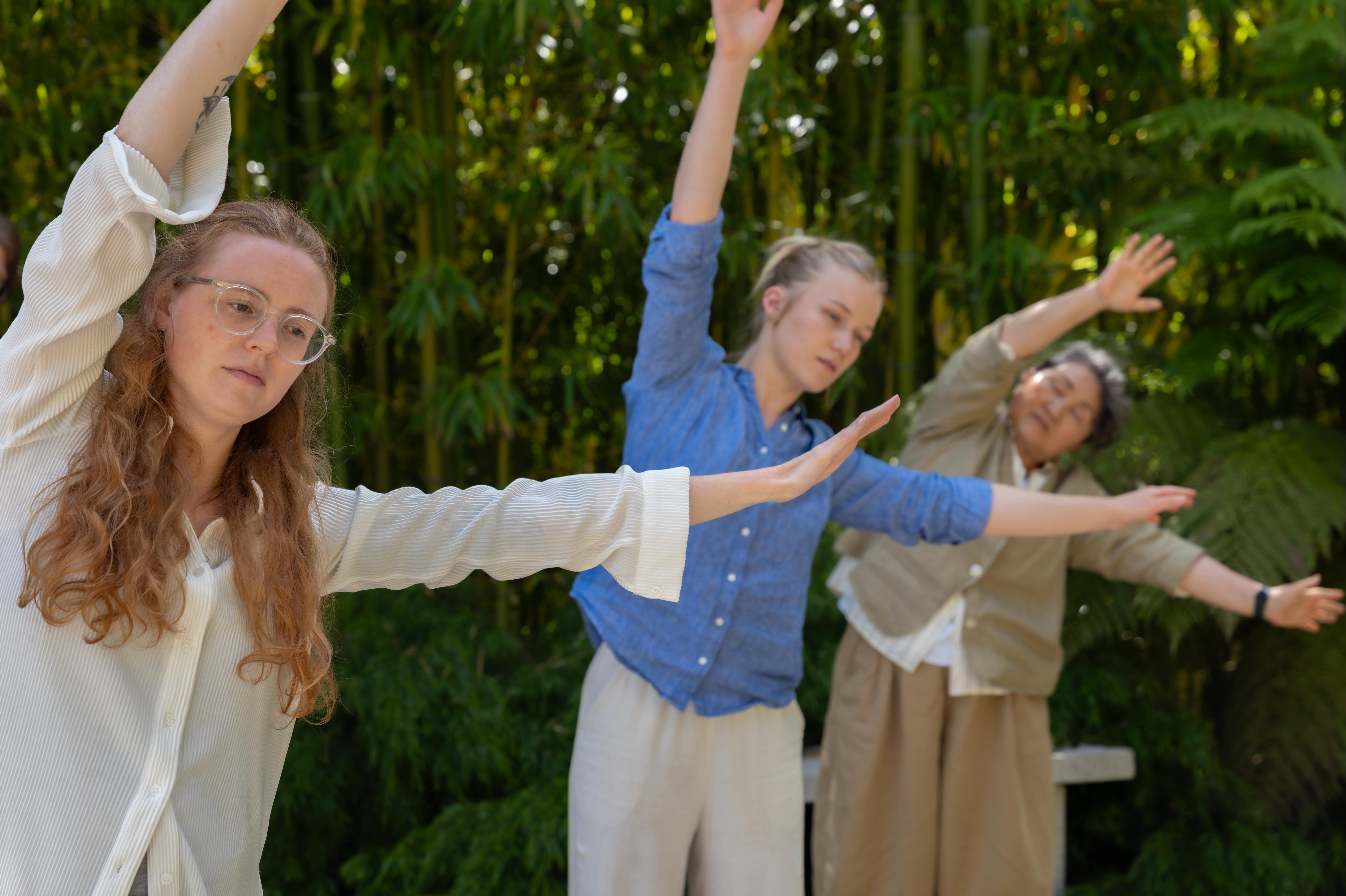 Three women practicing yoga outdoors in a lush green setting.