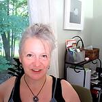 Portrait of a woman in a home office with books and a window view of trees.