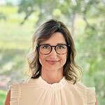 Woman with glasses smiling outdoors, representing community engagement.