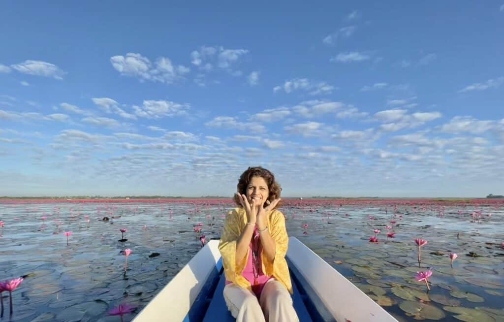 Woman sitting in a boat on a lake with pink water lilies and blue sky.
