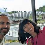 Two smiling people in front of a modern building with a curved roof.