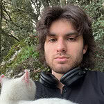 Young man holding a white cat outdoors in a wooded area.