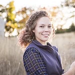 Young woman smiling holding wheat in a natural outdoor setting.