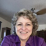 Smiling woman with curly gray hair in purple shirt indoors.