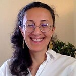 Smiling woman with glasses and earrings, indoors, representing community focus.