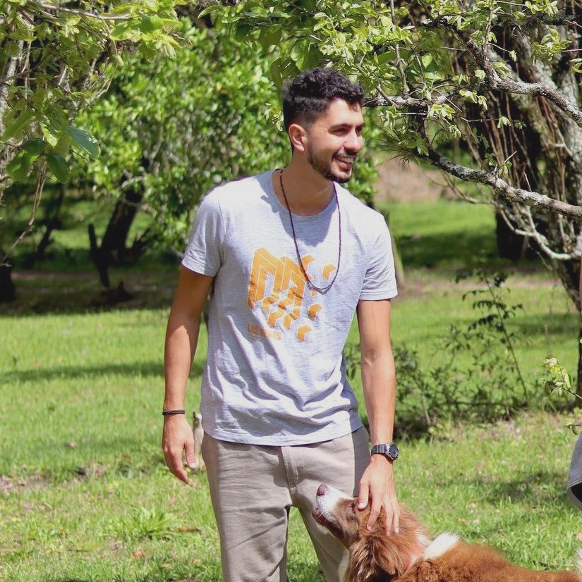 Man smiling outdoors with a dog in a green park setting.