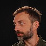 Profile of a man with a beard, nose piercing, and short brown hair.