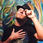 Person with black cap and black shirt in front of vibrant abstract mural.