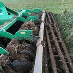 Green farming machinery working on soil preparation in a rural field.