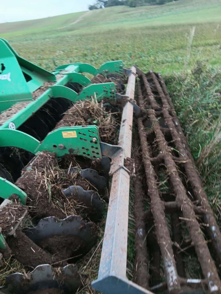 Green farming machinery working on soil preparation in a rural field.
