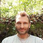 Smiling man in a forest setting for intentional community promotion.