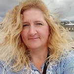 Portrait of a woman with blonde curly hair outdoors near water.