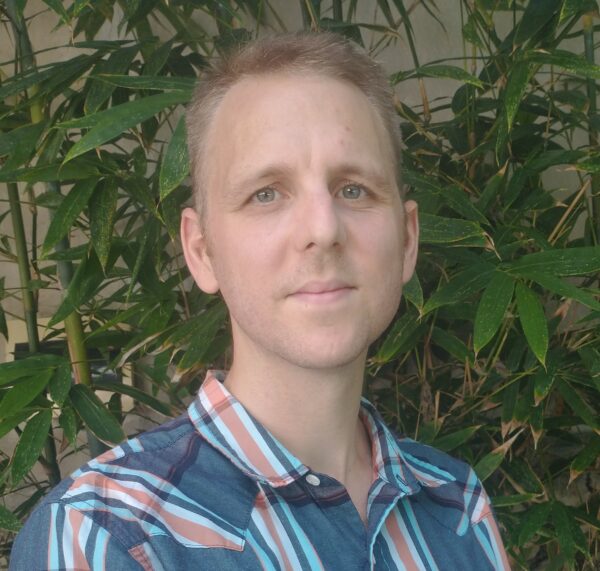 Portrait of a man outdoors with green foliage in the background.