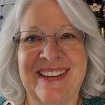 Smiling woman with gray hair and glasses, interior background.