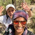 Two smiling women enjoying outdoor community event, one wearing sunglasses and a headscarf.